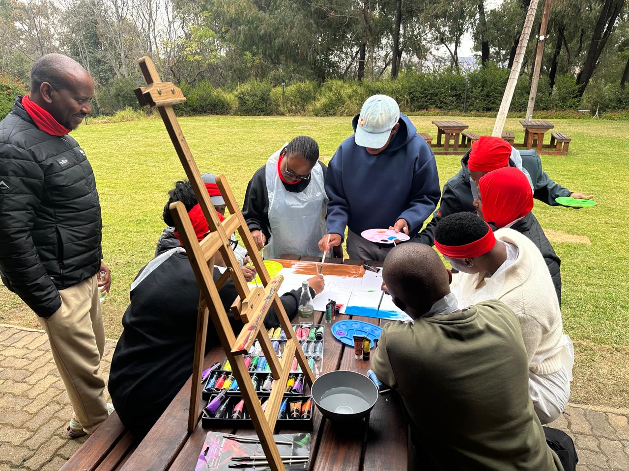 Team painting on easels together outdoors