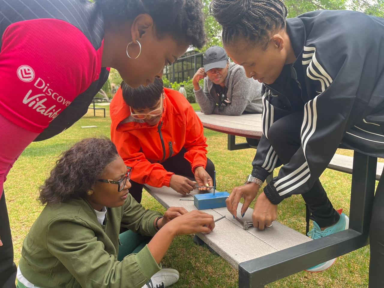 Team solving a nail-balance strategy puzzle at a picnic bench